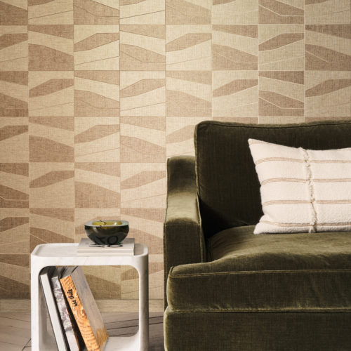 This inviting living space highlights the OAS231 reference, titled Domino, from Omexco’s Oase collection. The wallcovering is crafted from a patchwork of paperweave, where geometric shapes rest upon a metallic backing, available in gold or silver. The warm beige and earthy tones of the pattern enhance the organic aesthetic, perfectly complementing the deep green velvet sofa. A plush, textured cushion and a sculptural marble side table contribute to the balance of softness and structure, creating a sophisticated yet cozy atmosphere.