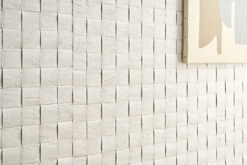 A striking close-up of Omexco's Pure collection, reference PU281, a bold wallcovering featuring a weave of mulberry bark that highlights the inherent richness and texture of this natural material. The intricate grid pattern creates a three-dimensional effect, adding depth and visual interest to the space. The natural tones of the bark are complemented by an abstract painting in muted hues, seamlessly blending the organic texture of the wallpaper with contemporary design elements. This combination celebrates the raw beauty of nature while enhancing the sophistication of modern interiors.