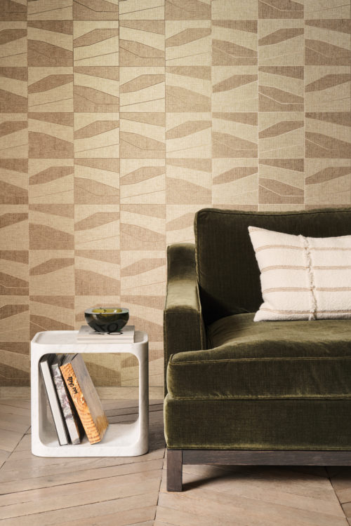 This inviting living space highlights the OAS231 reference, titled Domino, from Omexco’s Oase collection. The wallcovering is crafted from a patchwork of paperweave, where geometric shapes rest upon a metallic backing, available in gold or silver. The warm beige and earthy tones of the pattern enhance the organic aesthetic, perfectly complementing the deep green velvet sofa. A plush, textured cushion and a sculptural marble side table contribute to the balance of softness and structure, creating a sophisticated yet cozy atmosphere.
