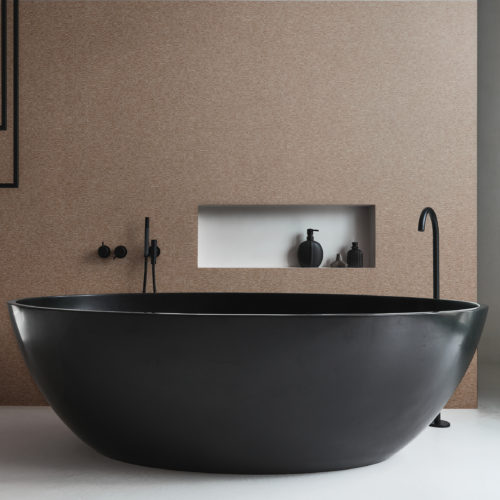 A luxurious bathroom featuring a striking black freestanding oval-shaped bathtub with modern taps and accessories. The walls are adorned with Omexco's high-performance wallcovering collection, Rivage, boasting textured tonal stripes in a captivating brown/red hue. The design adds a touch of sophistication and warmth to the space. Behind the bathtub, a niche in the wall provides a stylish storage solution.