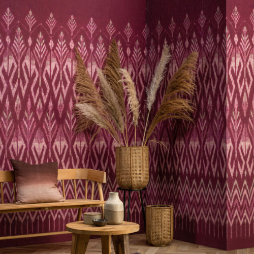 Tribu celebrates deeply authentic beauty as Omexco explores the art of weaving with paper. In this picture, we see the corner of a living room where the walls are decorated with a raspberry coloured ikat pattern.