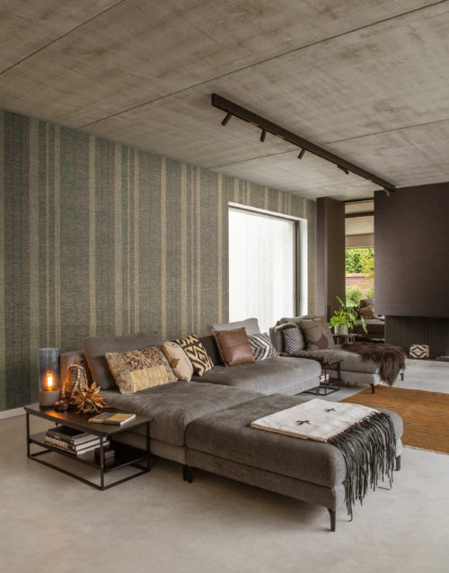 In this image we see a contemporary living room with a stunning rhythmic striped wall. This vibrant asymmetrical stripe is one of the designs of the Tribu wallcoverings by Omexco. A stunning paperweave collection.