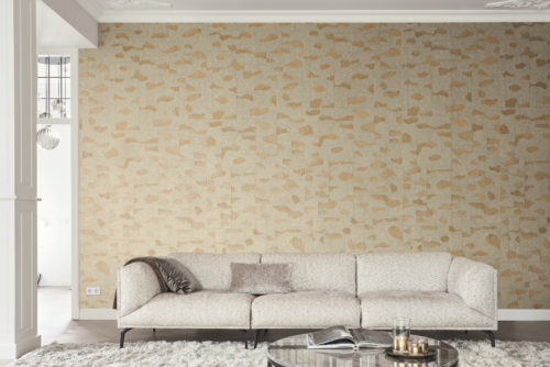 A spacious living room featuring high walls adorned with a classic ceiling strip. In the center, a comfortable beige sofa complements a stylish round marble coffee table. Behind the sofa, the wall is adorned with exquisite Omexco wallcoverings showcasing the Archipelago collection. This is a fine stardust wallcovering where mica is delicately printed with an organic design, evoking a sense of nature.