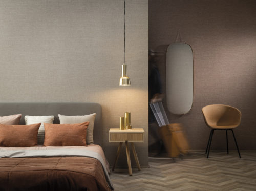 On the walls of this hotel room: the Abaca design in beige and blush hues from Omexco's High Performance Textures collection. It's a semi plain non-woven wallcovering with an intriguing texture, shown horizontally. The wallcovering is paired with a cosy bed, pendulum lamp, orange and beige pillows, orange chair and a wooden side table. Woven extra fine abaca. The abaca fibre we use as a grasscloth in Seraya and other collections is the inspiration.  It is the stem and supporting structure of the long leaves of the Abaca tree, a species of banana tree native to the Philippines.