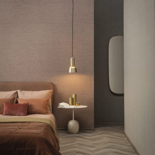 This image shows a hotel room decorated with Omexco's High Performance Textures wallcoverings in light pink and beige shades. The blush coloured pillows on the bed and wooden floor add a touch of warmth to the space.