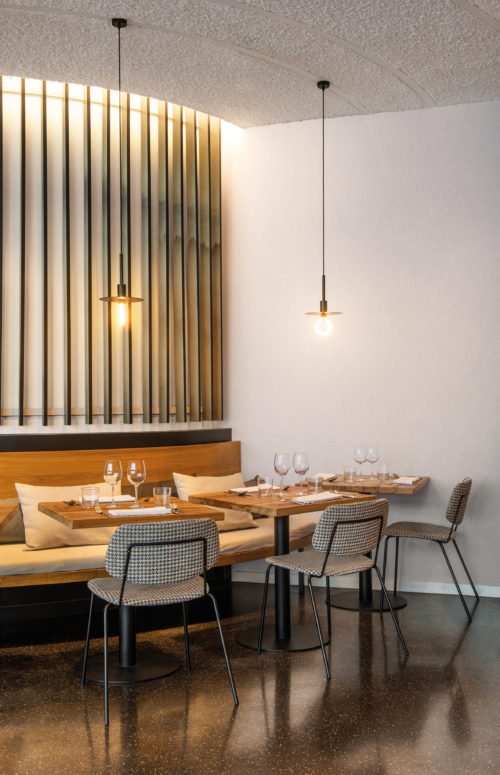 An eco-conscious solution for every project. The High Performance Patina Wallcovering collection by Omexco is created for residential, commercial and hospitality interiors all over the world. On the walls of this inviting, cosy restaurant nook with hanging bulb pendants we see the The “Chalk” design. This design, printed in off-white, is inspired by a special painting technique that creates a brushed chalk effect on the wall.
