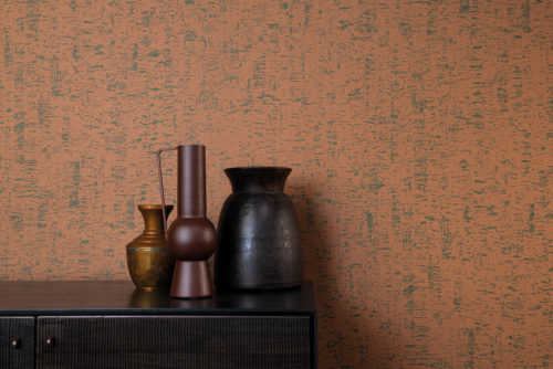 The High Performance Patina Wallcovering collection by Omexco combines performance with sustainability and modern aesthetics. This image shows an interesting printed non-woven wallcovering in burnt orange. The perfect backdrop for a dark brown wooden cupboard on which three metal vases in earth tones are posed. The wallcovering design,“ Clay”, is inspired by the clay walls and an old painting technique in which thin lime plaster is spread on the wall with a  block brush.
