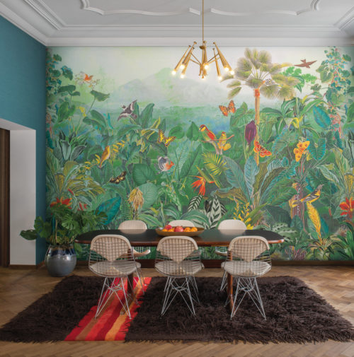 Here we see the impressive dining room of a Parisian style apartment, with a large wooden vintage dining table, six Eames Wire DKR Chairs, a modern golden chandelier, a heigh ceiling and herringbone parquet floor. But the true eye-catcher of the room is the wall showing a large jungle design with exotic plants, paradise birds and butterflies. This four drop panoramic design from Omexco’s "Birds of Paradise” collection is printed on non-woven wallcoverings and immerses us in nature’s splendour.