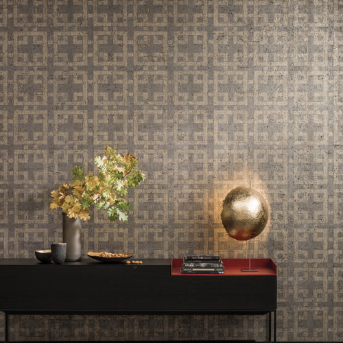 Low table with vase with oak branches, golden ball lamp, cork wallcovering with geometric design in the back.