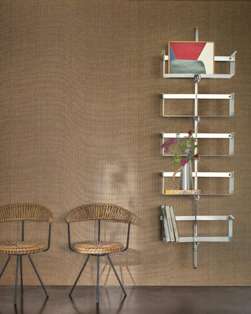 This refined interior highlights the OAS283 reference, titled Alma, from Omexco’s Oase collection. The wallpaper, crafted with meticulous paperweave craftsmanship, presents a timeless expression of artisanal excellence. The palette unfolds in three neutral tones, each inspired by the raw beauty and simplicity of nature. The textured surface adds warmth and depth to the space, seamlessly blending with the natural rattan chairs and the sleek, industrial-style shelving unit. A minimalist selection of books and a delicate floral arrangement complete the serene and harmonious ambiance.