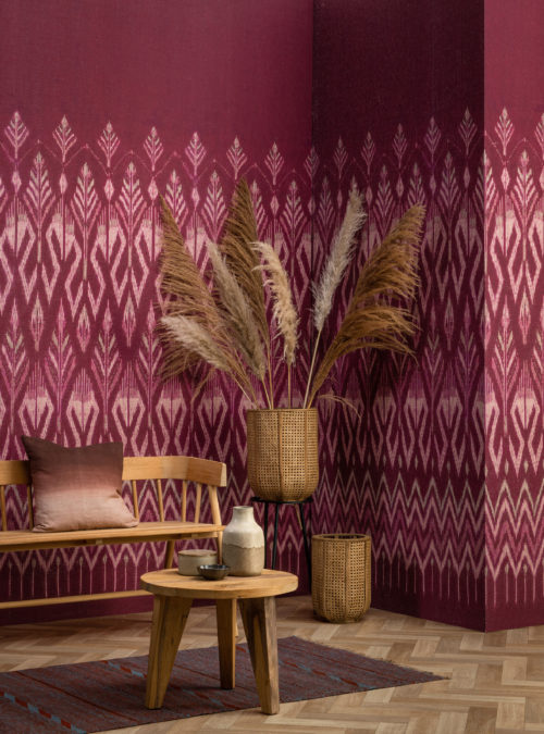Tribu celebrates deeply authentic beauty as Omexco explores the art of weaving with paper. In this picture, we see the corner of a living room where the walls are decorated with a raspberry coloured ikat pattern.