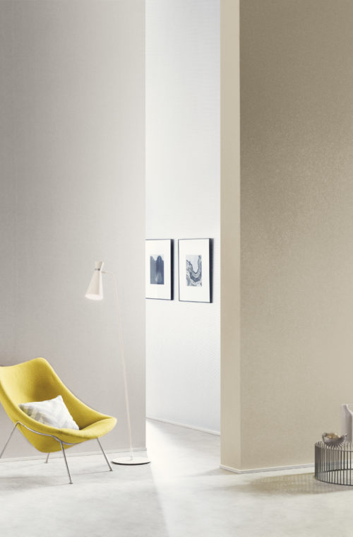 Intérieur contemporain très lumineux. Chaise jaune avec oreiller et liseuse. Nous regardons entre deux murs avec des revêtements muraux Kaléidoscope et voyons deux tableaux en noir et blanc.