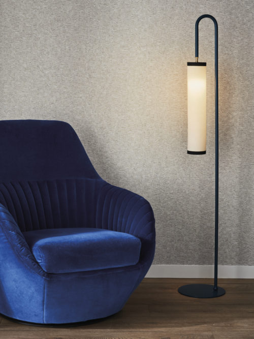 Gros plan d'un intérieur avec, à gauche, un fauteuil bleu en velours pelucheux et, à droite, un lampadaire minimaliste noir aux lignes épurées. Le sol est recouvert d'un parquet en bois. En arrière-plan, la collection haute performance Rivage d'Omexco sert de toile de fond, avec un design gris captivant et des rayures tonales texturées qui ajoutent de la profondeur et de l'intérêt visuel à l'espace. Ces revêtements muraux sont non seulement exempts de PVC et nettoyables à l'eau de Javel, mais ils offrent également des performances accrues en termes de facilité de nettoyage.