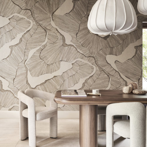 Un salon élégant avec une grande table à manger en bois entourée de confortables chaises beiges. Au-dessus de la table, trois grandes suspensions blanches ajoutent une touche moderne. À gauche, une fenêtre offre une vue sur un jardin avec des arbres, apportant une sensation de tranquillité à l'espace. Le mur est orné d'un design panoramique de la collection Café Society d'Omexco dans des nuances de brun très clair. Le design, imprimé numériquement sur du lin fin, fait une forte impression avec sa représentation de structures organiques.