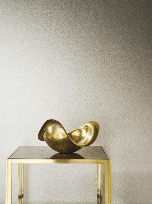 Les revêtements muraux en mica d'Omexco existent en différentes tailles. Sur cette photo, il s'agit de petits mica. La brillance des perles se marie bien avec la table en or et en verre et le bol en or.