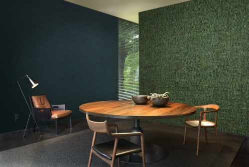 Salon avec fauteuil en cuir confortable et liseuse. Au mur, un revêtement mural Nomad uni d'un vert profond. Sur l'autre mur, un superbe revêtement marelle vert et noir.