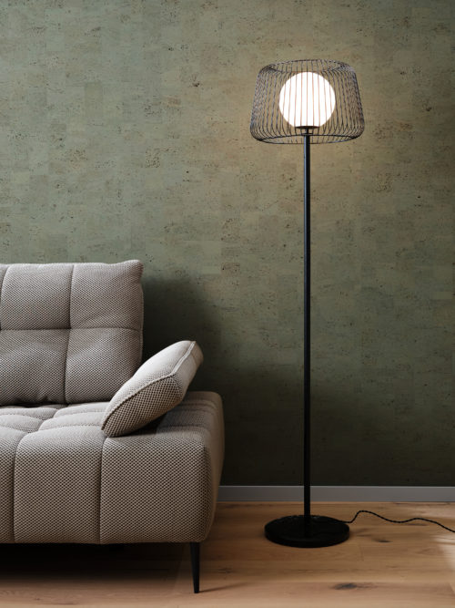 Image de décoration d'un canapé contemporain gris clair et d'un lampadaire en métal noir, tous deux posés sur un parquet brun clair. Le mobilier est adossé à un mur recouvert de la collection de revêtements muraux en liège "Casca" d'Omexco, de couleur vert mousse. Il s'agit d'un faux-uni, résultat d'un patchwork d'éléments rectangulaires en liège qui crée une variété de teintes sur le mur. La lumière du soleil projette une lueur chaude et dorée sur le sol et le mur.