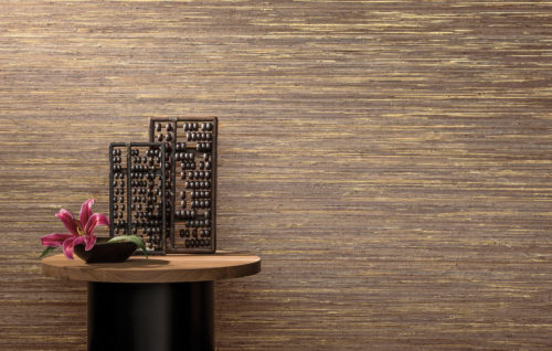 Magnifique revêtement mural en raphia doré. Petite table ronde avec deux abaques en bois et un vase ovale avec une fleur fuchsia.