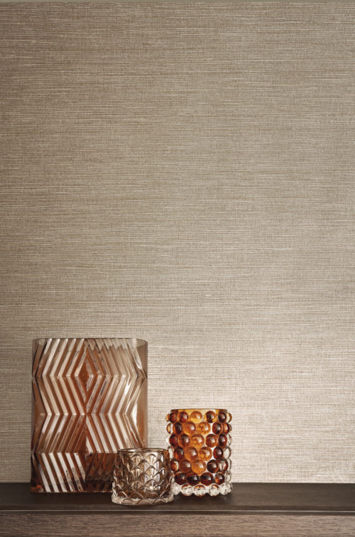 Un gros plan de décoration intérieure d'un plateau mural en bois avec trois vases en verre dans des tons d'orange et de marron. En arrière-plan, la collection de revêtements muraux en textile Café Society dans des nuances de rose doux. Il s'agit d'une réinterprétation de l'un des classiques les plus emblématiques d'Omexco, incarnant l'essence luxueuse de la soie à travers des fibres textiles méticuleusement imprimées.