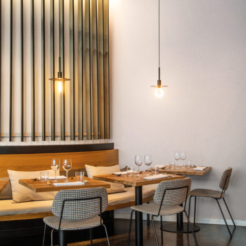 Une solution écologique pour chaque projet. La collection de revêtements muraux Patina haute performance d'Omexco est conçue pour les intérieurs résidentiels, commerciaux et hôteliers du monde entier. Sur les murs de ce coin de restaurant accueillant et confortable avec des ampoules suspendues, on peut voir le motif "Chalk". Ce motif, imprimé en blanc cassé, s'inspire d'une technique de peinture spéciale qui crée un effet de craie brossée sur le mur.