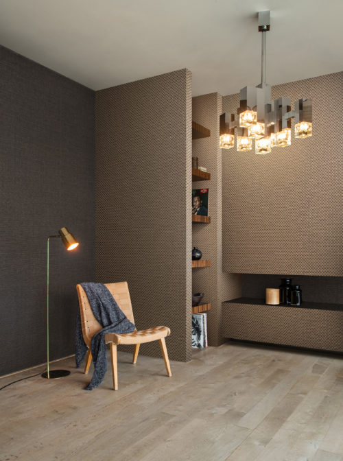 La collection Tribu d'Omexco répond à votre désir de modernisme multiculturel et de design intemporel. Sur cette image, nous voyons un coin salon moderne avec une chaise longue et des revêtements muraux en papier tissé d'une modernité saisissante dans des tons terreux.