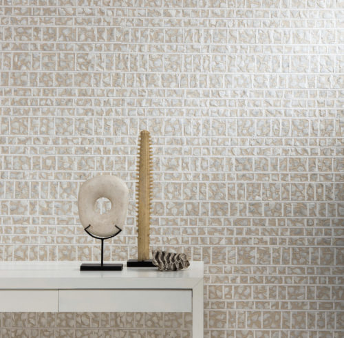 Gros plan sur une console blanche avec des œuvres d'art de la mer pétrifiée. Revêtement mural en capiz beige avec blocs blancs et nacre brillante.