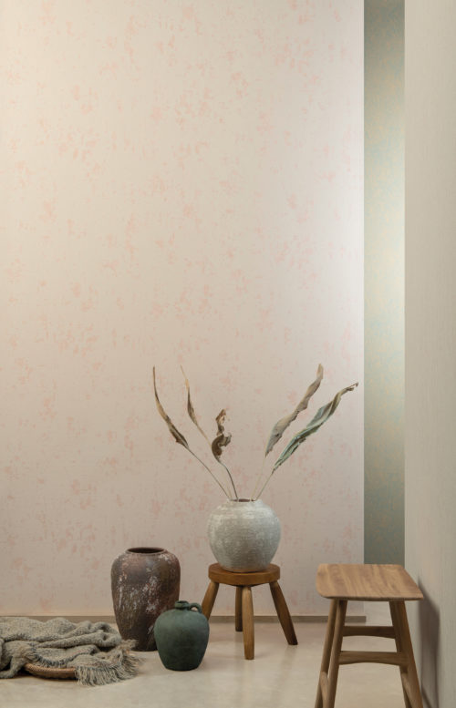 Un décor très zen où trois grands vases de forme organique et de finition mate attirent l'attention. L'un des vases contient des feuilles de plantes séchées. Deux tables d'appoint en bois naturel sont placées contre les murs. Les murs sont recouverts de revêtements muraux High Performance Patina d'Omexco en rose tendre. Le design s'inspire de la structure du grès. Très organique.