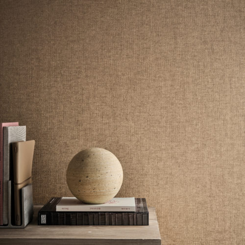 Cet intérieur raffiné met en avant la référence OAS283, intitulée Alma, issue de la collection Oase d’Omexco. Ce revêtement mural, réalisé selon une technique de tissage de papier sophistiquée, incarne un savoir-faire intemporel. Disponible en trois teintes neutres, chacune inspirée par la beauté naturelle et la simplicité de la terre, il apporte une texture chaleureuse et authentique à l’espace. Une console en bois minimaliste accueille une sélection de livres et d’objets soigneusement disposés, dont une sphère sculpturale en pierre qui fait écho à l’élégance brute du matériau.