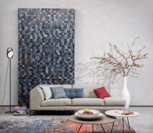 Décor équilibré avec le revêtement mural bakbak Borneo, le canapé avec des coussins bleus et rouges. Vase blanc avec des branches en fleurs. Deux tables basses rondes. Moquette aux reflets rouges et bleus.