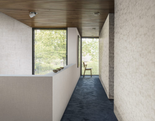 Couloir lumineux avec moquette verte/bleue. Sur les murs, 3 types de revêtements muraux blancs Omexco Aruba.