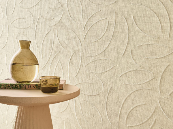 Cet intérieur apaisant met en avant la référence OAS221, Verano, issue de la collection Oase d’Omexco. Le revêtement mural, réalisé en tissage de papier raffiné, présente un motif brodé délicat inspiré de formes organiques, apportant un effet de mouvement et une touche sophistiquée à l’espace. Les tons neutres et doux créent une atmosphère accueillante et sereine, parfaitement rehaussée par une table d’appoint sculpturale, une carafe en verre et une tasse en céramique texturée. Le jeu de lumière et d’ombre sur la surface embossée accentue sa profondeur, en faisant un choix élégant pour des intérieurs naturels et raffinés.