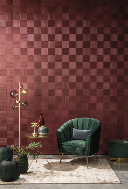 Le Gambit de la Reine a-t-il inspiré à Omexco ce revêtement mural exclusif appelé 'Chess' : glamour doux, harmonie subtile ? Sur cette photo, le design rouge de la marqueterie de bois exquise est associé à un fauteuil en velours vert contrastant et à des détails d'intérieur dorés.