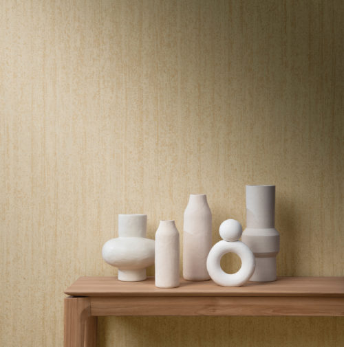 Gros plan sur une table basse en bois sur laquelle sont posés cinq vases en céramique de forme organique et de finition mate. Sur le mur, nous voyons la gamme de revêtements muraux High Performance Patina d'Omexco. Ce motif particulier, imprimé dans une couleur beige jaunâtre, est très texturé et s'inspire de la structure du bois brûlé, un aspect très populaire de nos jours.