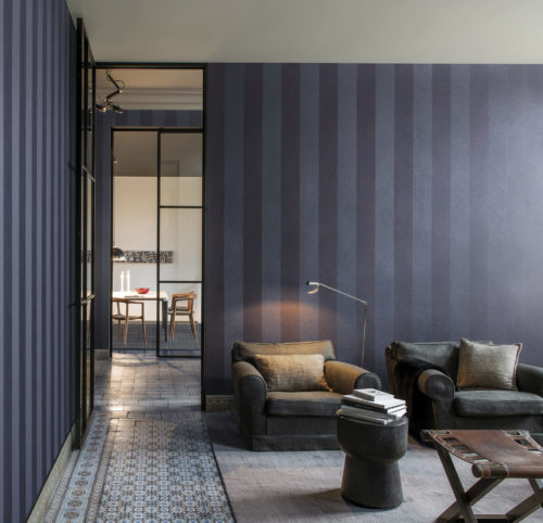 Salon avec deux fauteuils en linnen, des livres sur une table d'appoint. Revêtement mural à chevrons bleus.