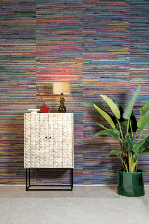 Un décor tropical avec un sol et une moquette beiges, un bananier exotique, une armoire en bois à deux portes sur un cadre métallique minimal et une lampe de table éclairée avec abat-jour. Mais ce qui attire vraiment l'attention dans cette pièce, c'est le revêtement mural extrêmement coloré de l'atelier de collection d'Omexco : de la soie de sari recyclée est torsadée en rubans et tissée à la main avec des ficelles de papier. La texture faite à la main vous remplit de joie et de beauté.