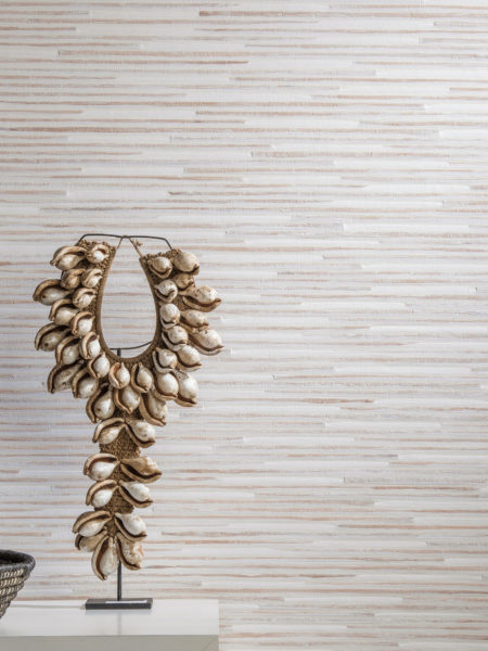 Détail d'un nénuphar et d'un revêtement mural en papier tissé dans des tons blancs et nus. Œuvre d'art avec des coquillages sur une console blanche.