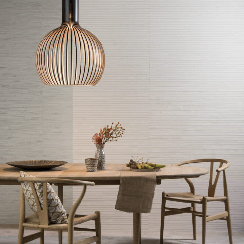 Table en bois d'aspect naturel avec deux chaises Wegner en forme de triangle. Un cadre parfait pour les revêtements muraux naturels Shades of Pale d'Omexco.