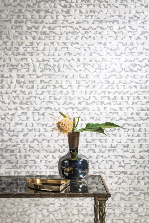 Une table en verre foncé reflétant le revêtement mural capiz gris et blanc de la collection Shades of Pale.