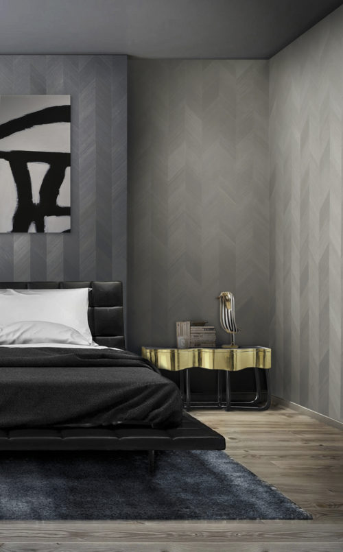 Chambre à coucher avec un lit en cuir noir et une table de nuit dorée. Tableau noir et blanc sur le mur. Murs habillés d'un revêtement mural en placage bois de la gamme Omexco Infinity.