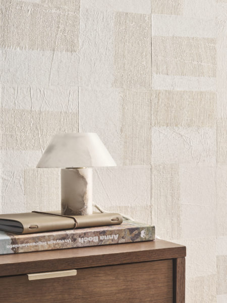 Un intérieur raffiné mettant en avant la collection Pure d’Omexco, référence PU261, un revêtement mural nommé Intensify, présentant un patchwork géométrique en papier enrichi d’un tissage ajouré d’abaca aux tons de lin. Ce design apporte de la profondeur, de la texture et une dimension tactile à l’espace, créant un point focal visuel remarquable. La scène comprend un meuble en bois minimaliste avec une poignée en laiton discret, surmonté d’une pile de livres et d’un carnet en cuir, reflétant une organisation soignée. Une lampe de table en marbre au design sculptural renforce l’esthétique luxueuse mais épurée. La combinaison harmonieuse de textures organiques et de motifs géométriques fait de ce papier peint un élément central pour des intérieurs modernes et sophistiqués.