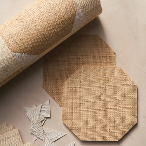 Un gros plan sur la référence PU431 de la collection Pure, mettant en avant la marqueterie sophistiquée du raphia. L’image présente un rouleau de revêtement mural avec un motif géométrique en fibres naturelles, des panneaux octogonaux soigneusement découpés et de petits morceaux triangulaires. La texture du matériau souligne la précision artisanale et l’aspect organique du revêtement mural. Un éclairage doux met en valeur les teintes naturelles et le caractère fait main de la composition.