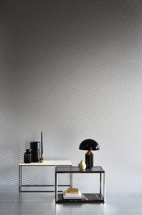 Intérieur contemporain avec deux tables carrées en métal et des accessoires blancs et noirs. Sur les murs, un revêtement mica argenté satiné avec des vagues en relief. Le revêtement a été posé horizontalement, ce qui lui donne un aspect plus moderne.