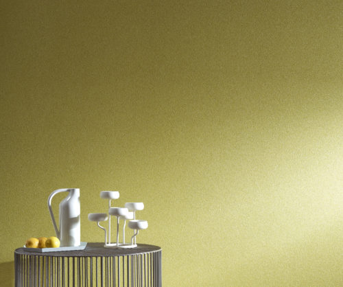 Table contemporaine en fil de fer avec vase et bougeoirs blancs. Le jaune des citrons sur la table se retrouve dans le revêtement mural jaune graphite.