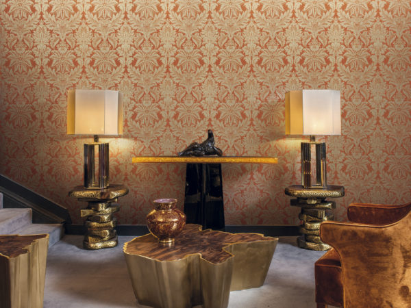 Chambre tactile avec fauteuil brun, lampes dorées et table centrale. Revêtement mural damassé or et orange de Gala.