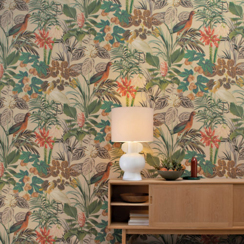 Exemple d'une pièce avec un sol en bois à chevrons et des revêtements muraux tropicaux. Le motif botanique du revêtement mural se compose de feuillages, de fleurs et d'échassiers. Ici, sur un fond beige, on voit un ibis orange et une spatule blanche. Il s'agit des exubérants revêtements muraux "Oiseaux de paradis" d'Omexco. Devant le mur tropical, nous voyons un buffet en bois sur lequel sont posés une lampe de table blanche et un bol avec de petits ananas.