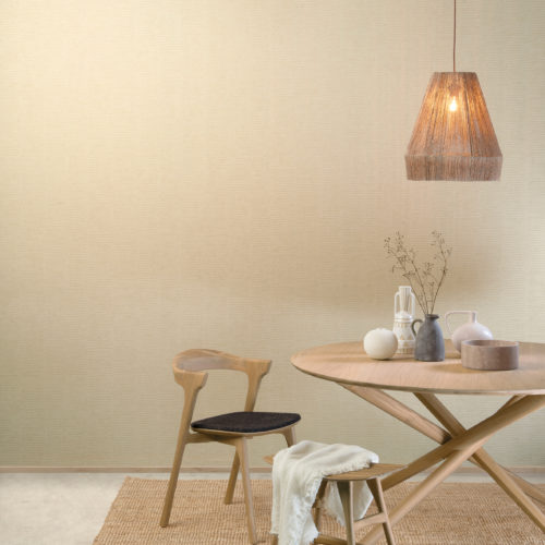 La collection de revêtements muraux High Performance Patina d'Omexco allie performance, durabilité et esthétique moderne. Sur le mur de cette salle à manger accueillante, nous voyons un imprimé beige de rayures verticales combinées à des lignes horizontales. L'espace est meublé d'une table et de chaises de style scandinave, marquées par des lignes simples et épurées et par le minimalisme.