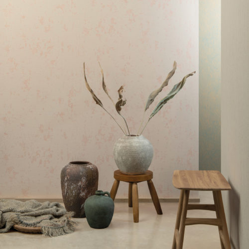 Un décor très zen où trois grands vases de forme organique et de finition mate attirent l'attention. L'un des vases contient des feuilles de plantes séchées. Deux tables d'appoint en bois naturel sont placées contre les murs. Les murs sont recouverts de revêtements muraux High Performance Patina d'Omexco en rose tendre. Le design s'inspire de la structure du grès. Très organique.