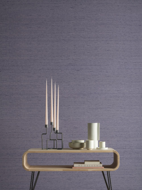 Nous voyons un gros plan étonnant avec une table d'appoint en bois et des éléments décoratifs modernes tels que des bougies et des vases. La toile de fond parfaite pour la texture violette du design Tussah des revêtements muraux High Performance Textures d'Omexco. La fonction rencontre la beauté, la durabilité rencontre le luxe, la durabilité rencontre la haute performance. La soie Tussah est plus épaisse et plus résistante que la soie ordinaire. Elle est facilement reconnaissable à ses brins de soie plus épais qui ressortent dans le tissage.