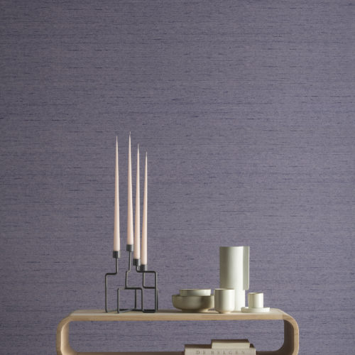 Nous voyons un gros plan étonnant avec une table d'appoint en bois et des éléments décoratifs modernes tels que des bougies et des vases. La toile de fond parfaite pour la texture violette du design Tussah des revêtements muraux High Performance Textures d'Omexco. La fonction rencontre la beauté, la durabilité rencontre le luxe, la durabilité rencontre la haute performance. La soie Tussah est plus épaisse et plus résistante que la soie ordinaire. Elle est facilement reconnaissable à ses brins de soie plus épais qui ressortent dans le tissage.