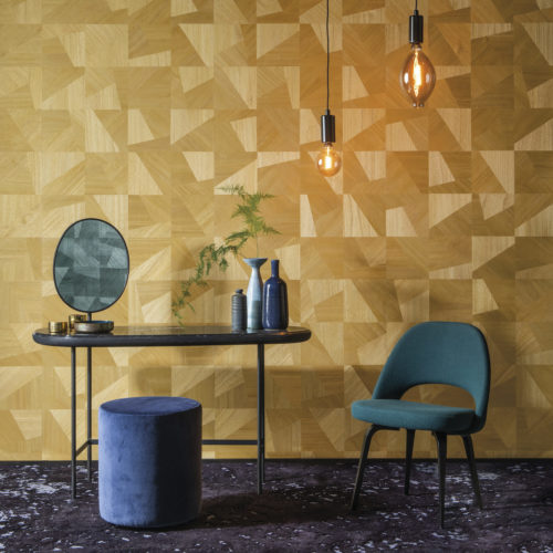 Cette photo illustre la façon dont la collection Omexco Sycamore incarne la beauté naturelle et le glamour doux. Un beau contraste entre les dimensions jaunes du design des textures de bois chic imbriquées et les détails verts de l'intérieur : une chaise, un pouf, des lampes à suspension et, dans le miroir, on voit apparaître le même revêtement mural en vert.